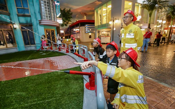 Children in firefighter uniforms using hoses at Kidzania Bangkok.