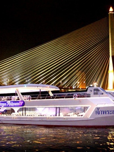 Dinner cruise boat on Chao Phraya River with illuminated bridge in Bangkok.