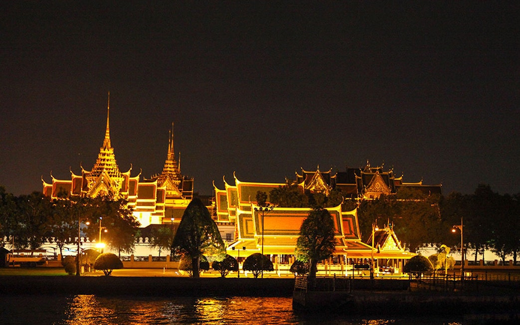Grand Palace illuminated at night, viewed from Chao Phraya River in Bangkok.