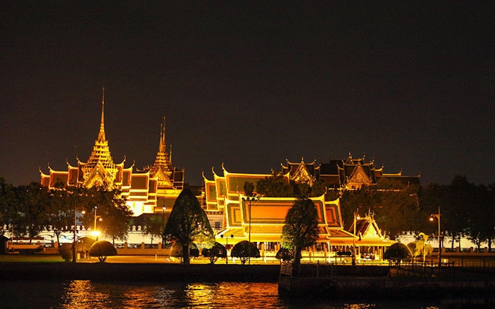 Grand Palace illuminated at night, viewed from Chao Phraya River in Bangkok.