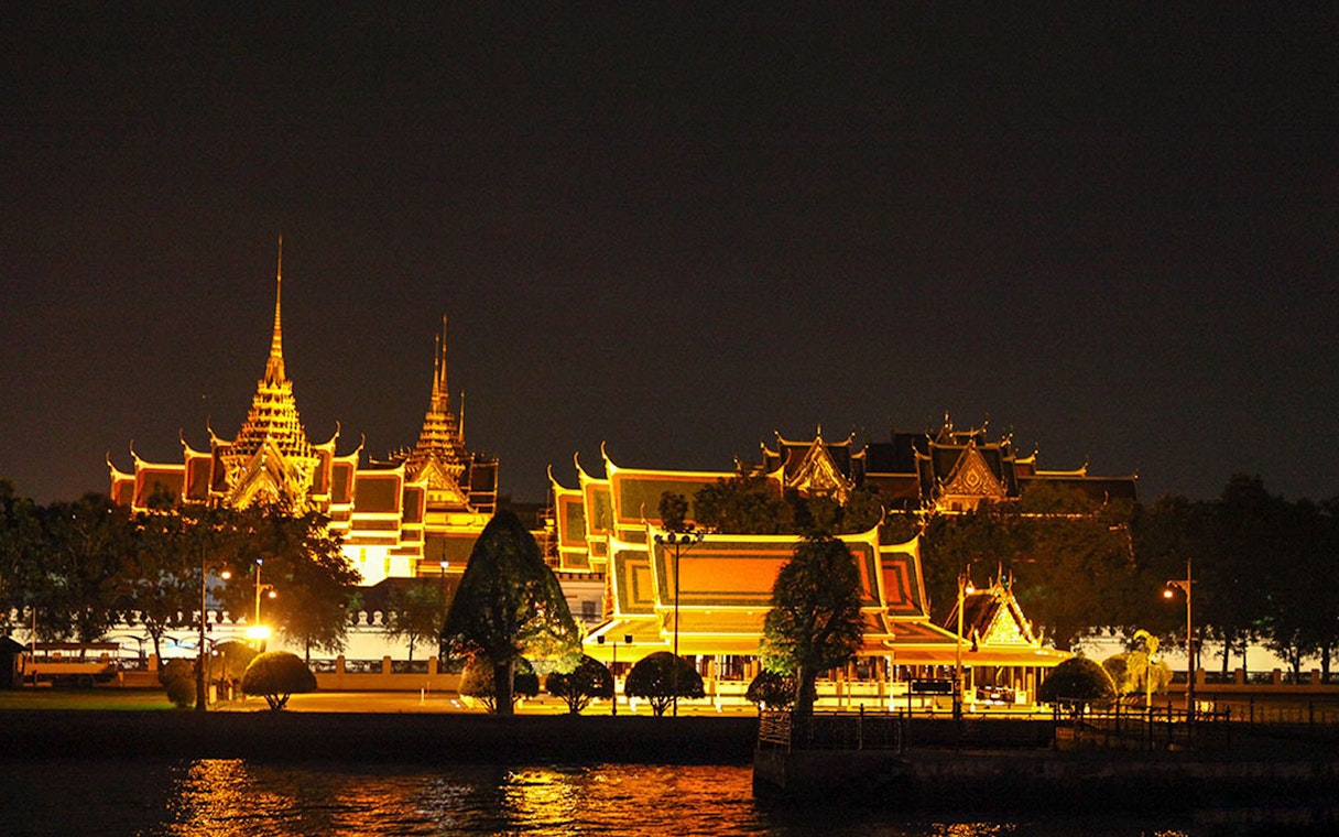 Grand Palace illuminated at night, viewed from Chao Phraya River in Bangkok.