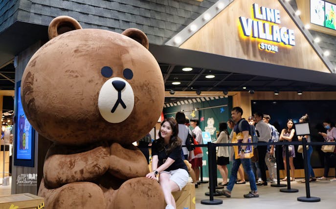 Giant bear statue at LINE Village Bangkok entrance with visitors in line.