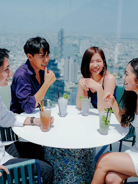 Group enjoying drinks at Mahanakhon SkyWalk with Bangkok skyline in the background.