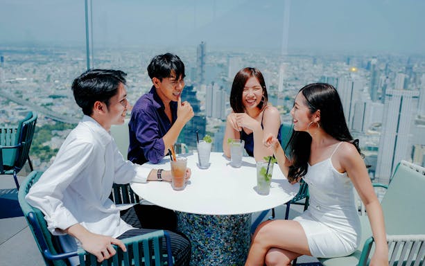 Group enjoying drinks at Mahanakhon SkyWalk with Bangkok skyline in the background.
