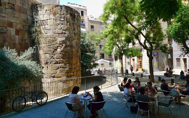 Barcelona Gothic Quarter, people dining outdoors near ancient stone wall.