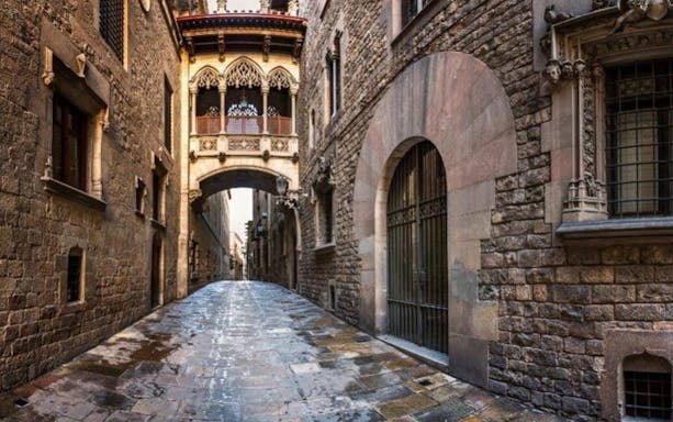 Barcelona Gothic Quarter street with stone buildings and a historic bridge overhead.