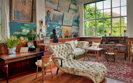 Giverny Monet's studio with paintings and floral furniture, view of garden through large window.