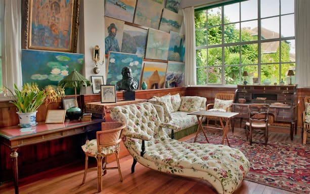 Giverny Monet's studio with paintings and floral furniture, view of garden through large window.