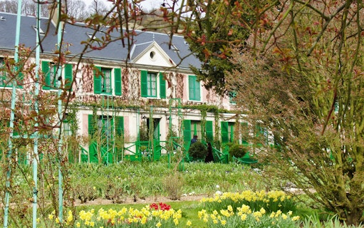 Giverny Monet's house with vibrant gardens, featuring blooming flowers and green shutters.