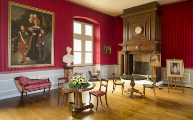 Interior of a room at Clos Lucé Castle with red walls, antique furniture, and historical portraits.