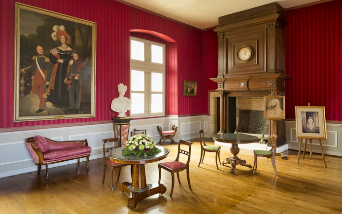 Interior of a room at Clos Lucé Castle with red walls, antique furniture, and historical portraits.