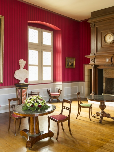 Interior of a room at Clos Lucé Castle with red walls, antique furniture, and historical portraits.
