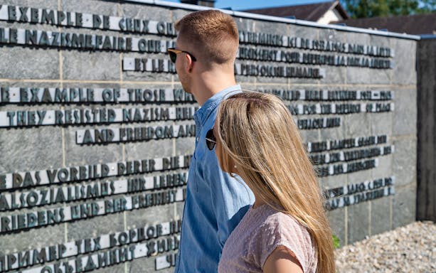Visitors reading memorial wall at Dachau Concentration Camp, part of Munich tour.
