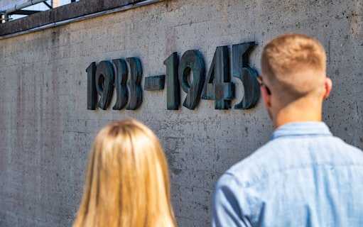 Visitors viewing the 1933-1945 memorial wall at Dachau Concentration Camp.