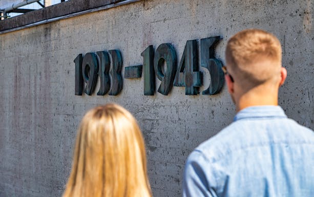 Visitors viewing the 1933-1945 memorial wall at Dachau Concentration Camp.