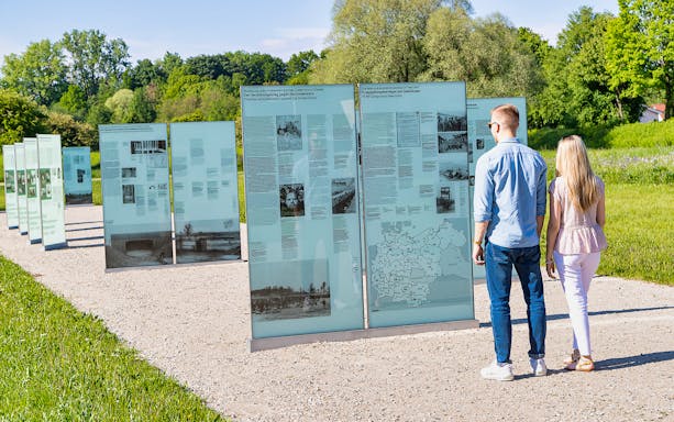 Visitors reading outdoor exhibits at Dachau Concentration Camp Memorial site.