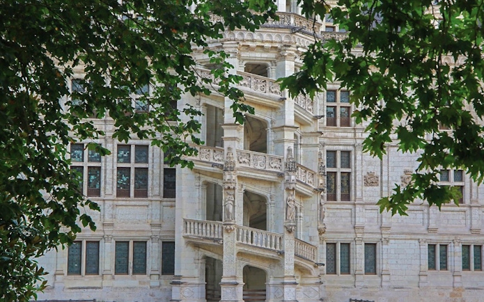 Renaissance staircase at Château de Blois, France, framed by green leaves.