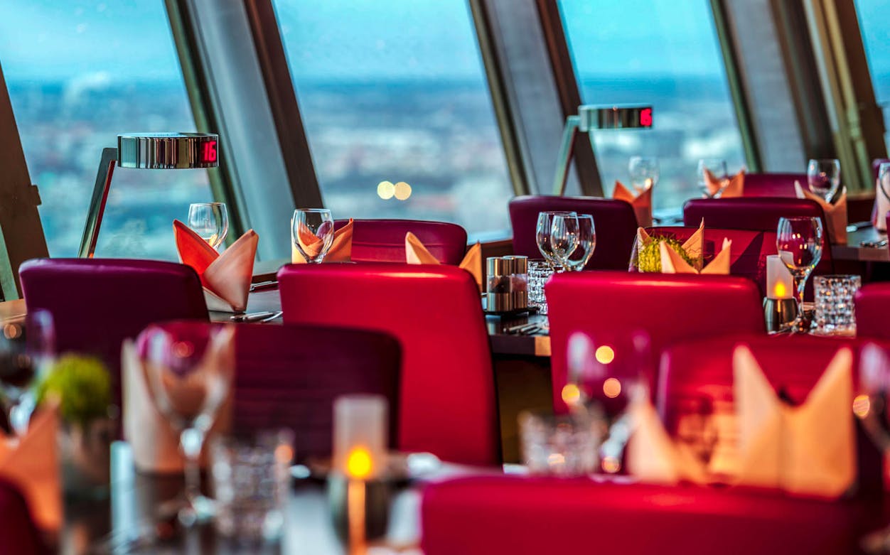 Dining tables set at Berlin TV Tower restaurant with city view.