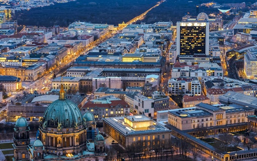 Aerial view of Berlin cityscape at dusk from the TV Tower, highlighting illuminated streets and buildings.