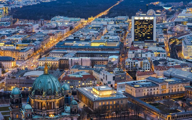 Aerial view of Berlin cityscape at dusk from the TV Tower, highlighting illuminated streets and buildings.