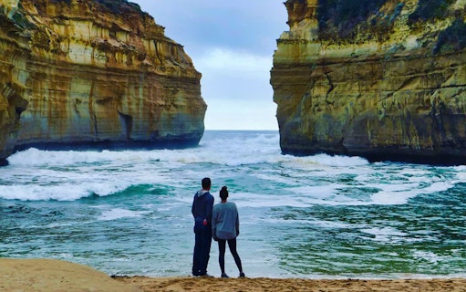 Couple viewing ocean waves between cliffs on Great Ocean Road tour.