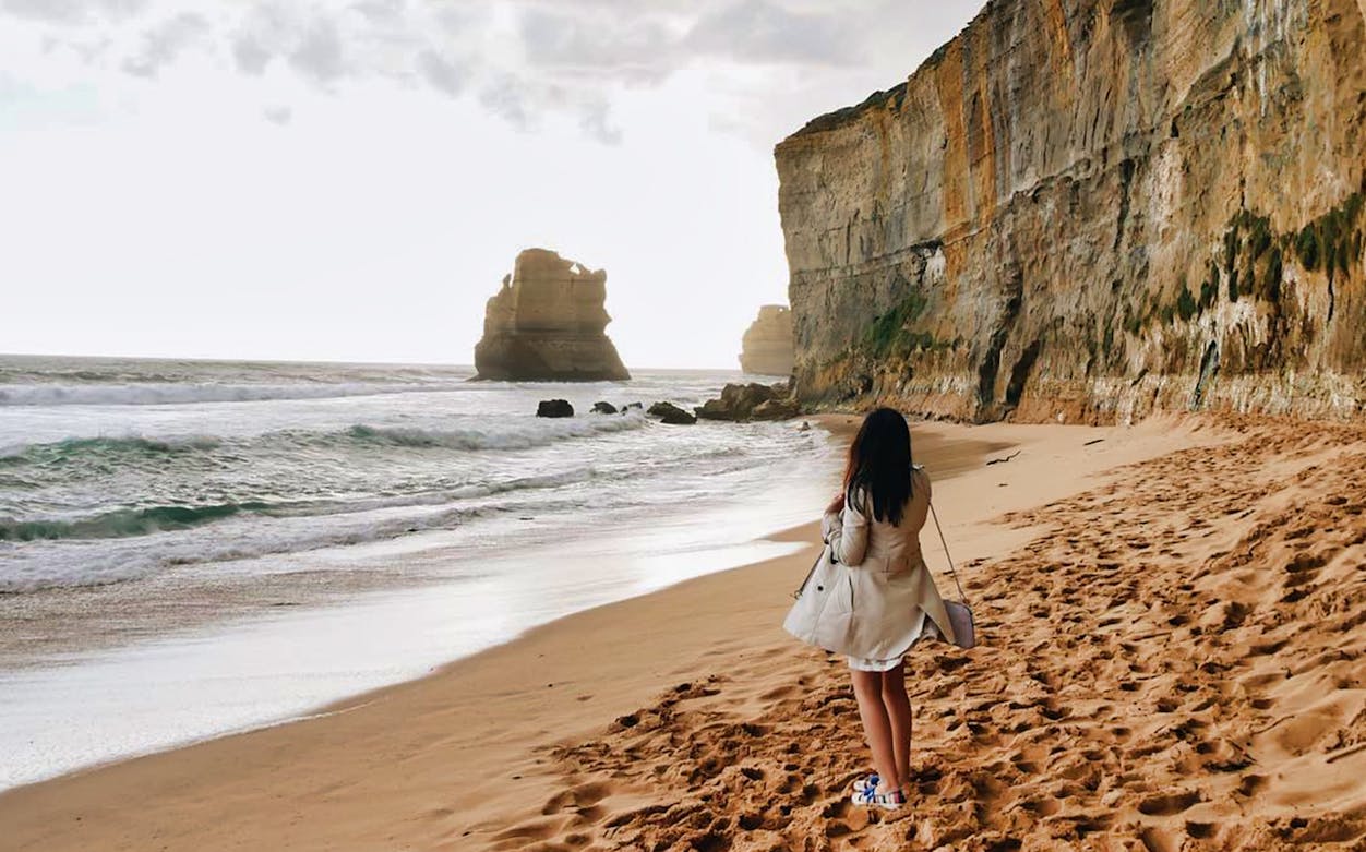 Woman walking along the beach near cliffs on the Great Ocean Road at sunset.
