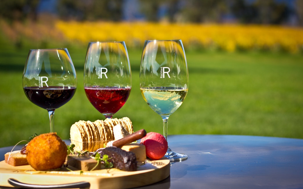 Three wine glasses with red and white wine, cheese platter at Yarra Valley vineyard.