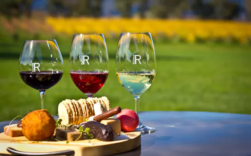Three wine glasses with red and white wine, cheese platter at Yarra Valley vineyard.