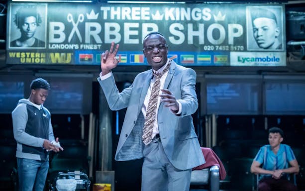 Man in a suit performing in front of a barbershop sign, related to Barber Shop Chronicles.