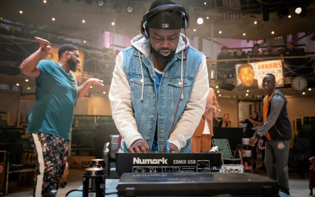 DJ performing at Barber Shop Chronicles event with audience in background.