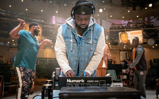 DJ performing at Barber Shop Chronicles event with audience in background.