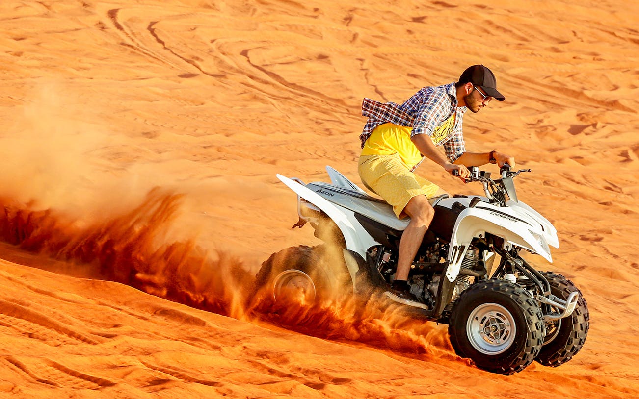 Person riding a quad bike on red desert dunes during a 1-hour tour.