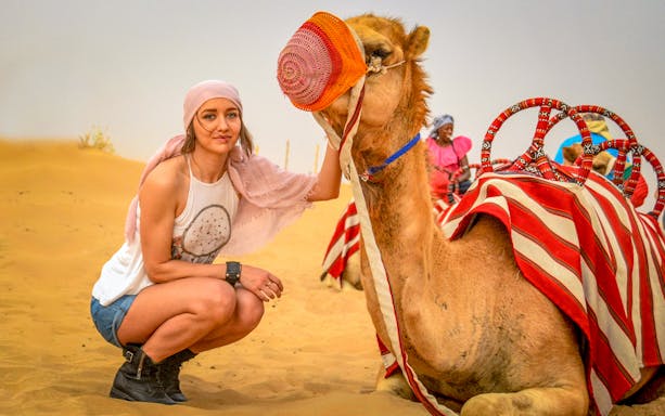 Camel ride experience in desert with a woman petting a camel, part of 50 min quad biking tour.