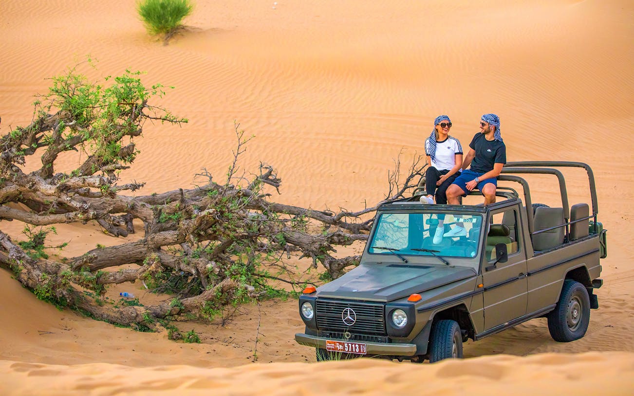 Visitors sitting on a vintage Mercedes in Al Marmoon Oasis desert safari.
