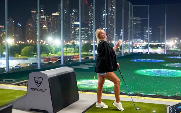 Person enjoying Topgolf with city skyline view during a Hop-On Hop-Off Tour.