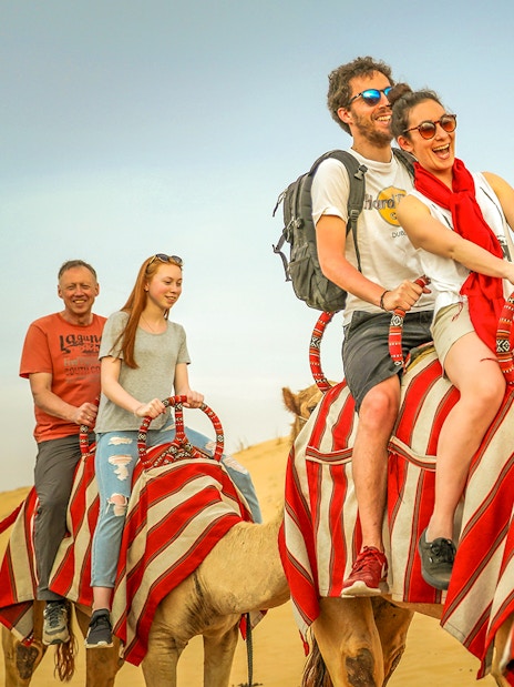 Tourists riding camels in the desert during an all-inclusive Bedouin safari with sunrise trek.