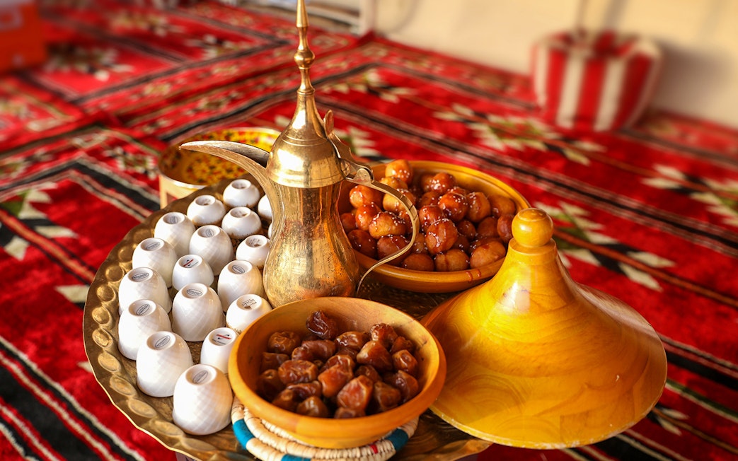 Traditional Bedouin tea set with dates and sweets on a patterned rug during desert safari.