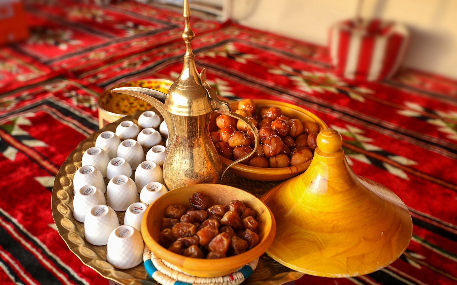 Traditional Bedouin tea set with dates and sweets on a patterned rug during desert safari.