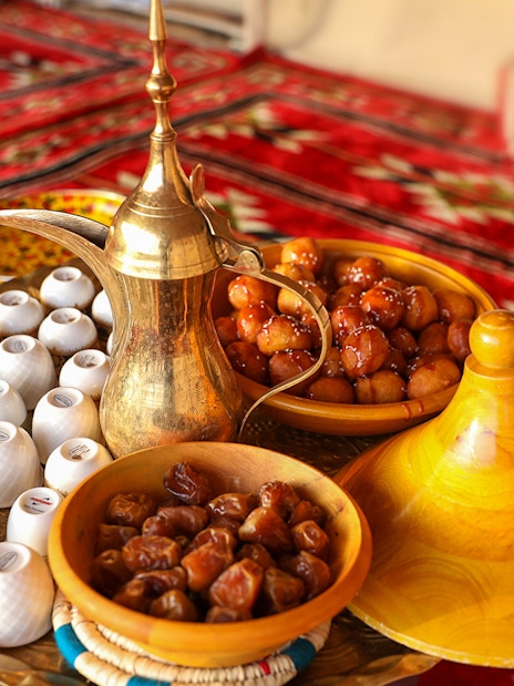 Traditional Bedouin tea set with dates and sweets on a patterned rug during desert safari.