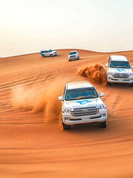 Desert safari SUVs driving over sand dunes during Bedouin desert tour.