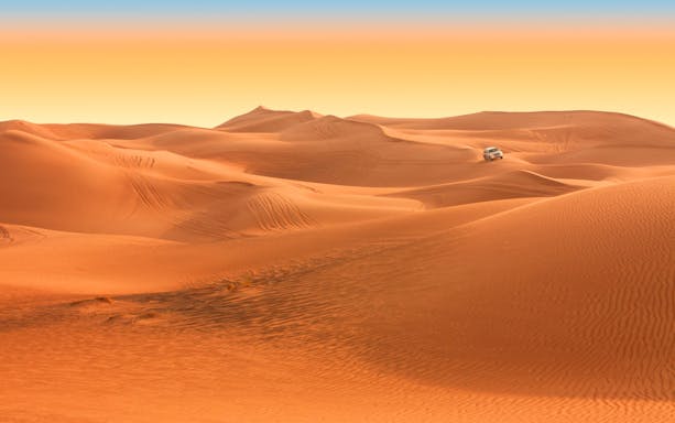 SUV driving across vast Arabian desert dunes during safari tour.