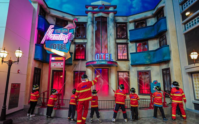 Children in firefighter uniforms practicing at Kidzania Seoul's Flamingo Hotel exhibit.
