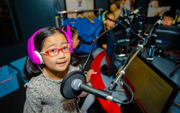 Child wearing headphones at Kidzania Seoul radio station exhibit.