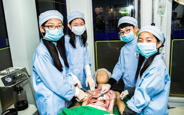 Children in surgical attire performing a mock operation at Kidzania Seoul.