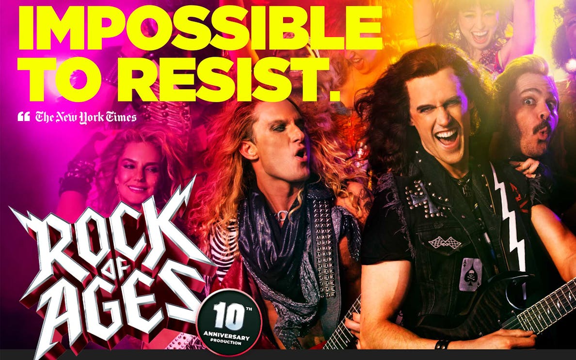 Rock of Ages performers playing guitars on stage with vibrant lighting.