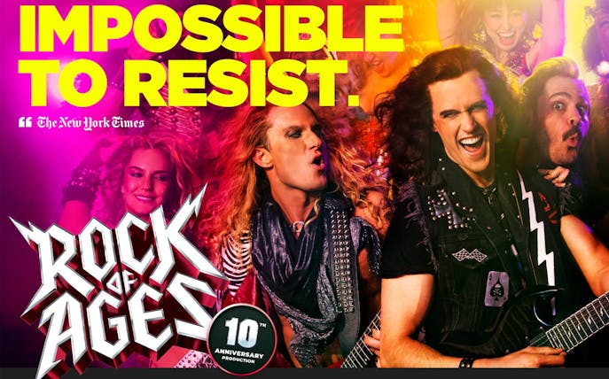 Rock of Ages performers playing guitars on stage with vibrant lighting.