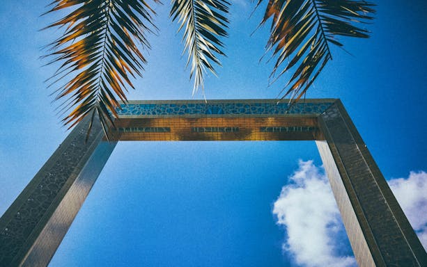 Dubai Frame viewed from below with palm leaves against a blue sky.