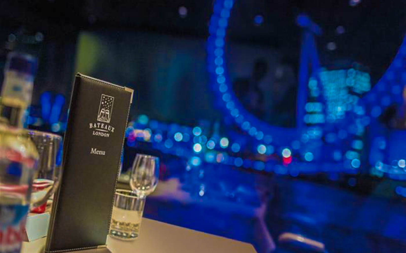 Bateaux London menu on table with blurred view of London Eye in background.