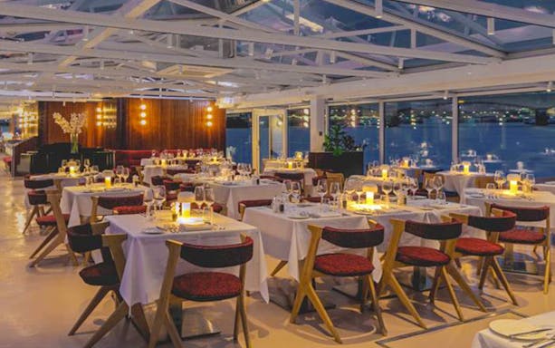 Dining area on Bateaux London cruise with tables set for dinner on the Thames.