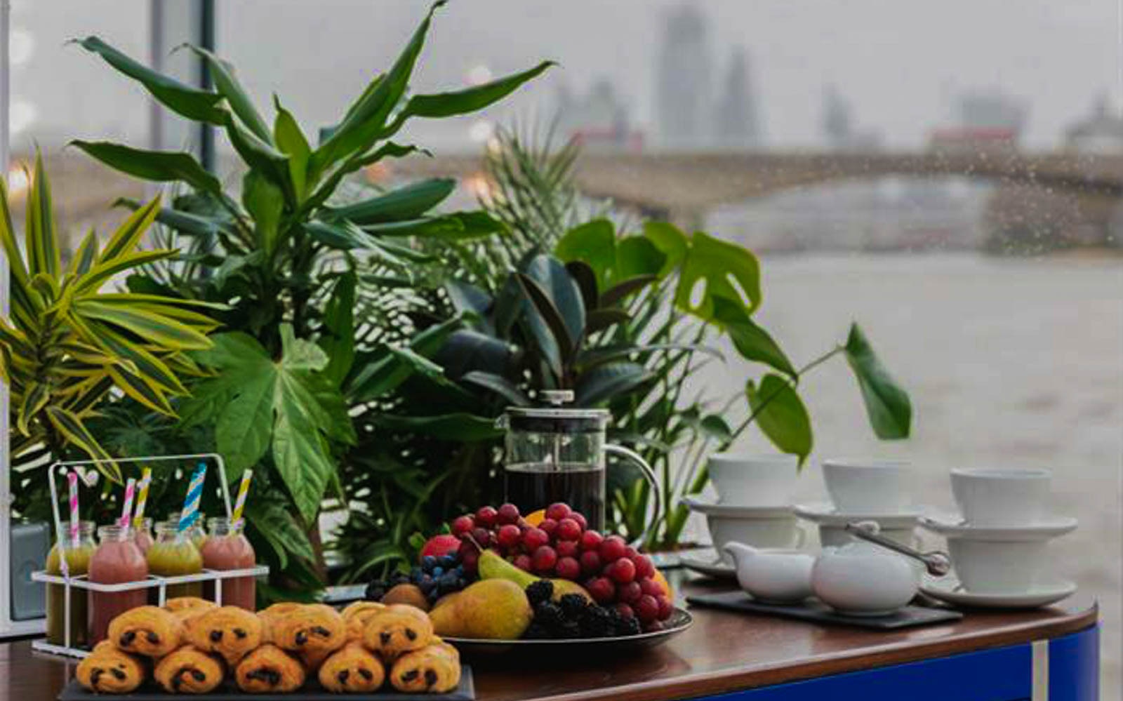 Pastries and fruit on a table with River Thames view during Bateaux London Lunch Cruise.